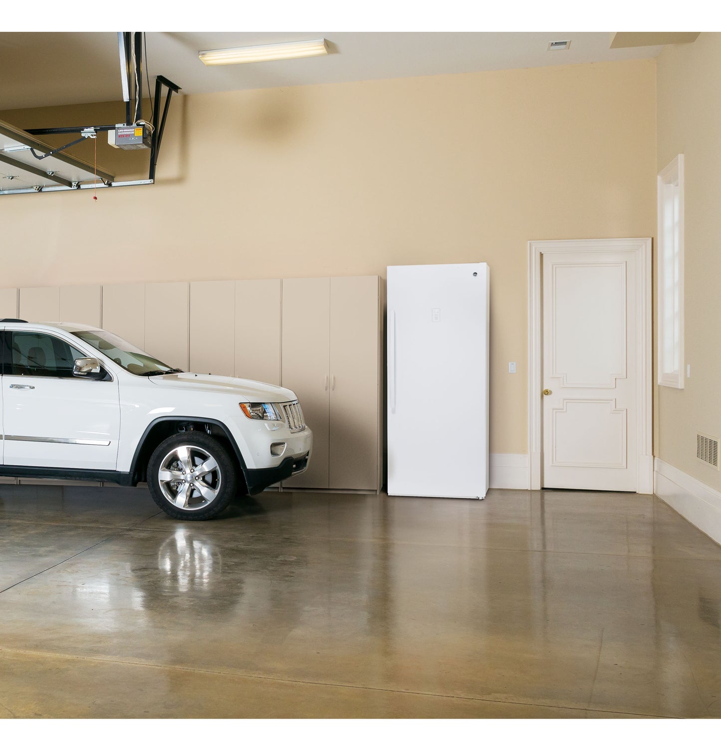 White upright frost-free freezer with vertical handle placed in clean garage with parked white SUV, storage cabinets, and closed door
