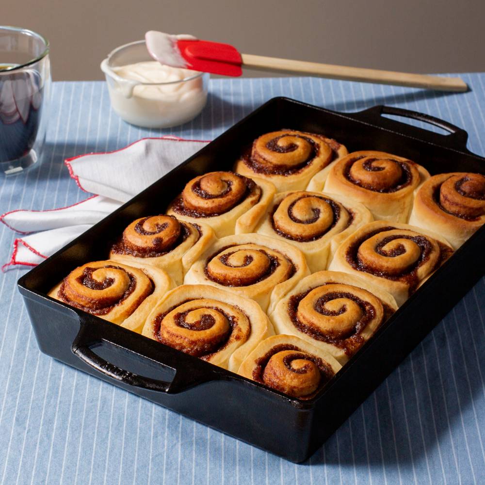 Black cast iron casserole pan with handles holding freshly baked cinnamon rolls in kitchenware collections