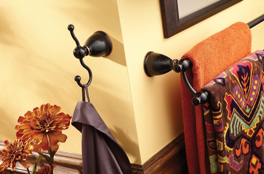 Mediterranean bronze double robe hook mounted on wall next to towel rack with colorful towels and decorative flowers