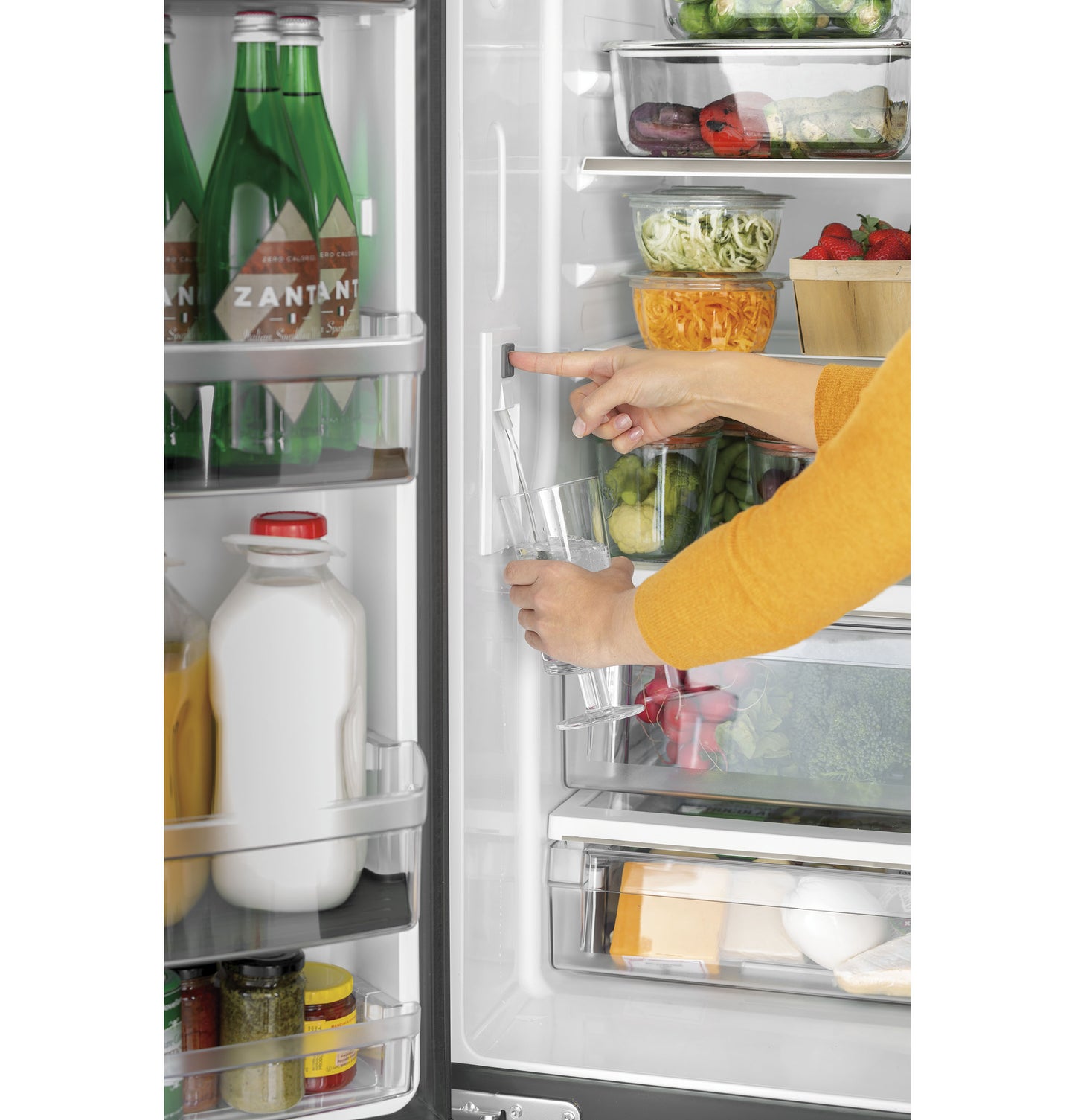 Hand pressing water dispenser button and filling glass inside stainless steel counter-depth French-door refrigerator with fresh food items