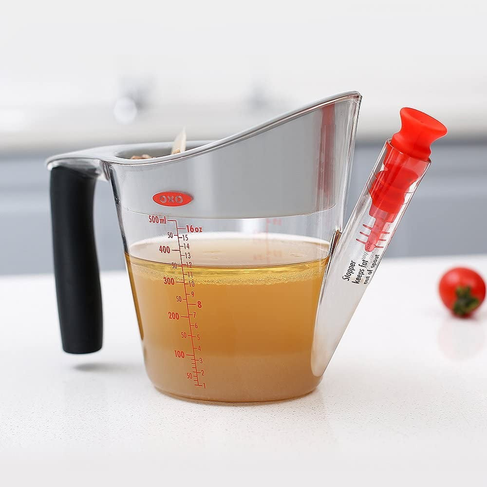Clear fat separator with black handle and red stopper filtering broth for kitchen gadgets and kitchenware collections
