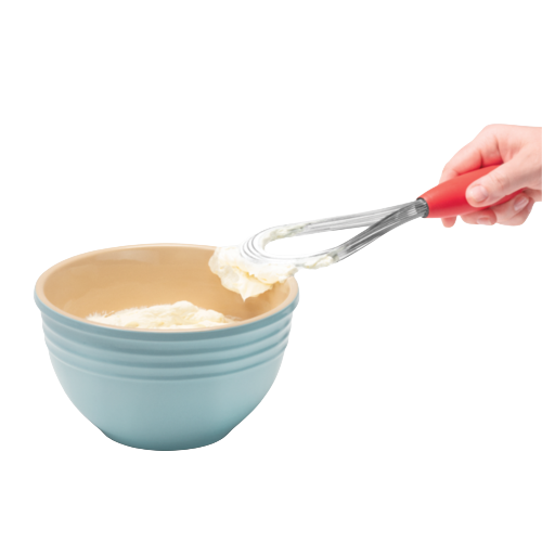 Hand holding red-handled stainless steel Flisk scraping batter from blue ceramic mixing bowl in kitchen utensil setting