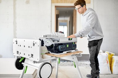 Man setting up a Festool cordless table saw on a portable stand inside a home improvement workspace