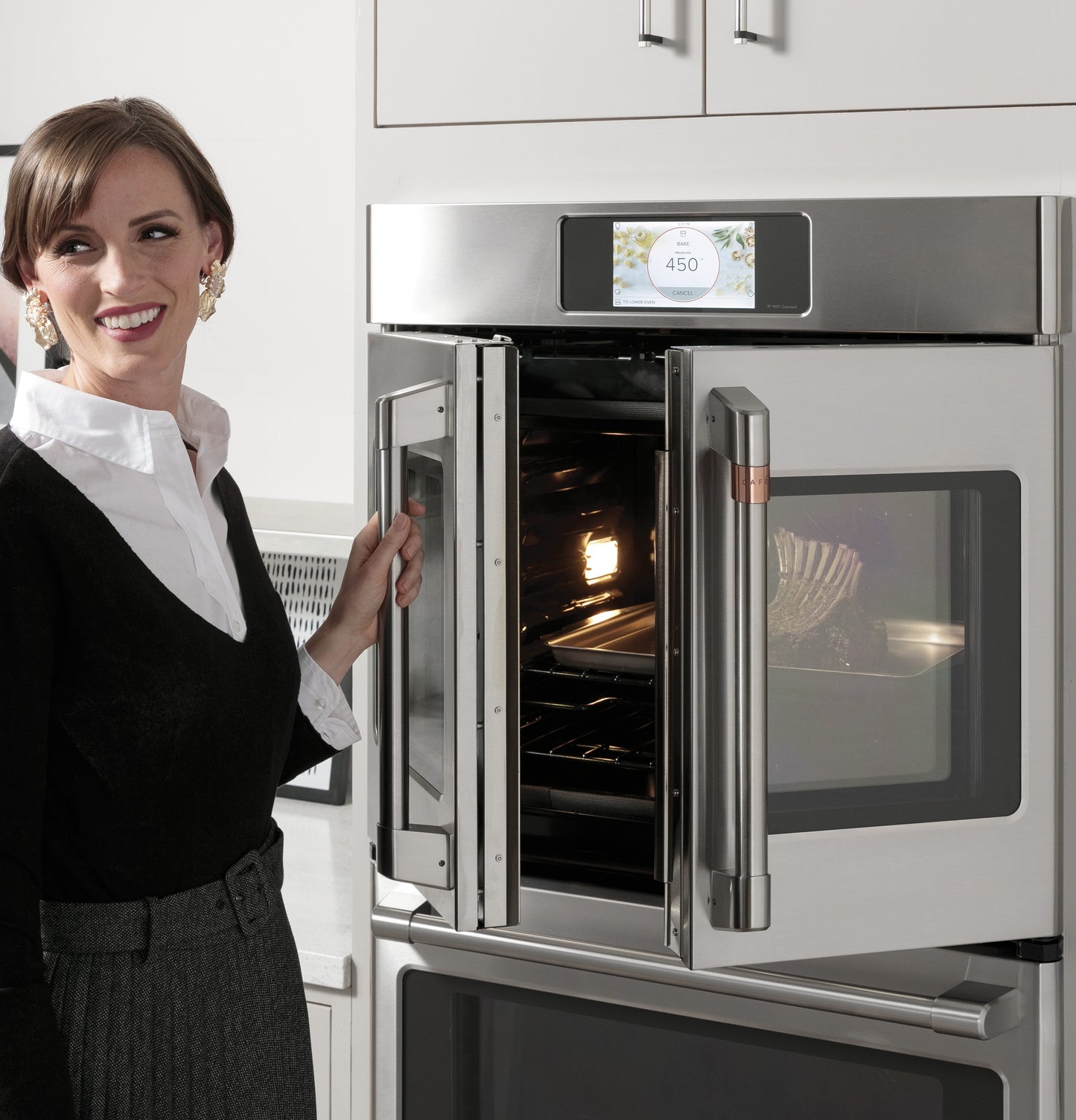 Woman stands beside open stainless steel double wall oven with touch screen in modern kitchen setting