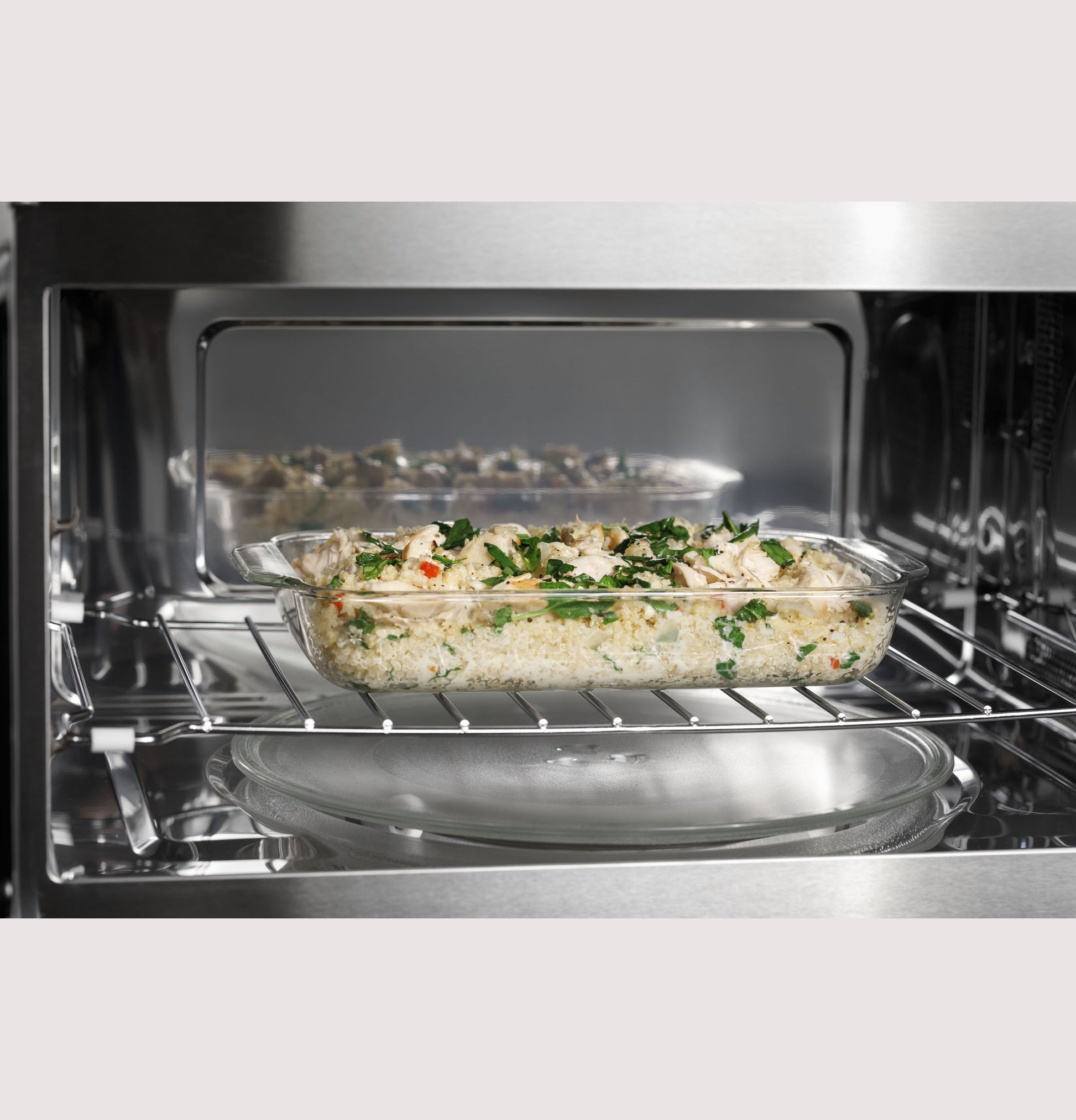 Glass baking dish with seasoned rice and herbs cooking on wire rack inside convection microwave oven interior
