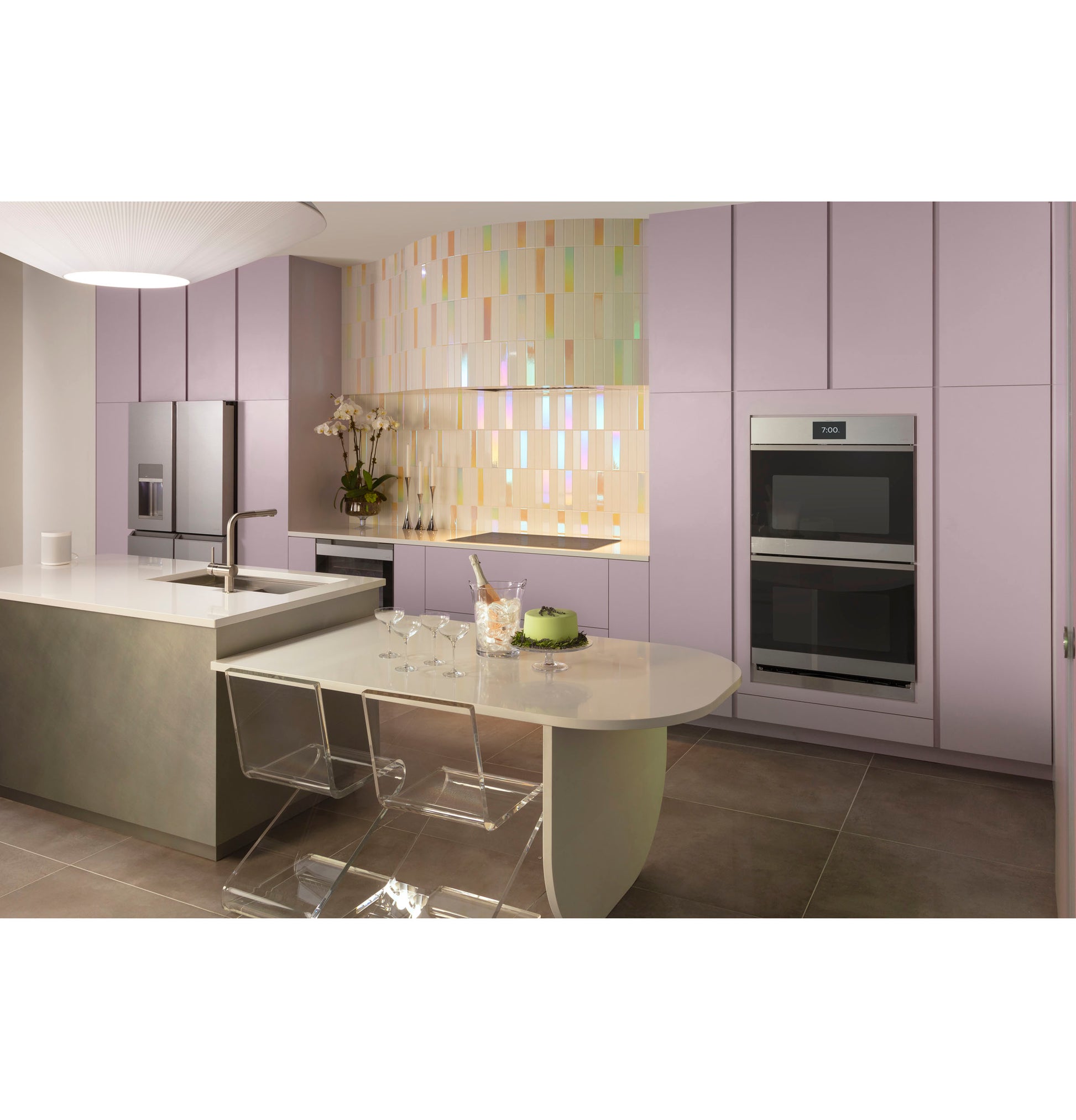 Modern kitchen with lavender cabinetry, built-in double ovens, transparent dining chairs, and iridescent tiled backsplash