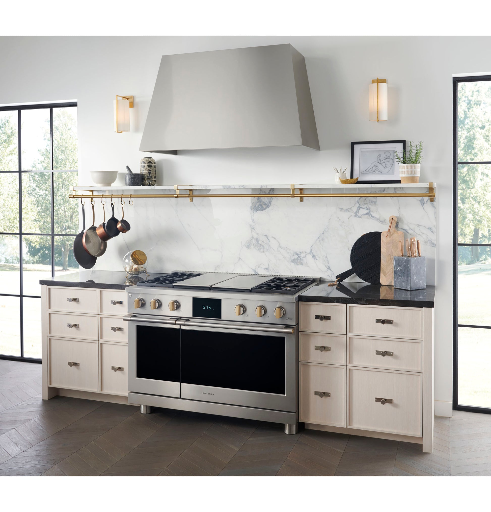 Contemporary kitchen with custom stainless steel range hood, light cabinetry, marble backsplash, and brass cookware rail