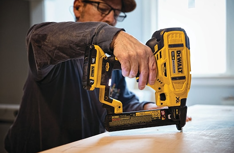 Worker using yellow and black cordless narrow crown stapler for home improvement on wooden surface