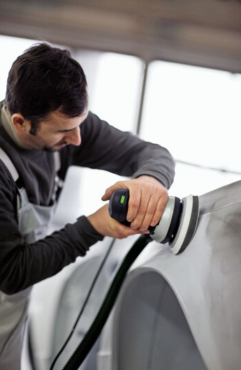 Man using power sander with dust extraction for auto body refinishing in a workshop setting