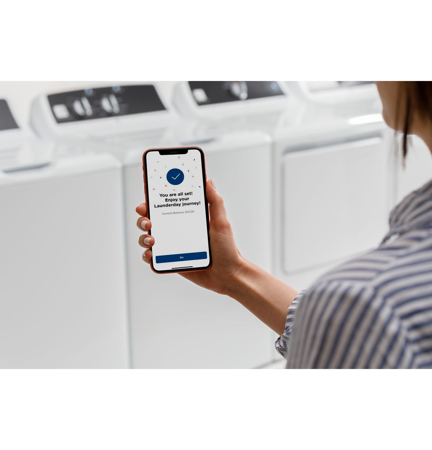 Person holding smartphone with app confirmation screen in front of white commercial top load washers from washers collection