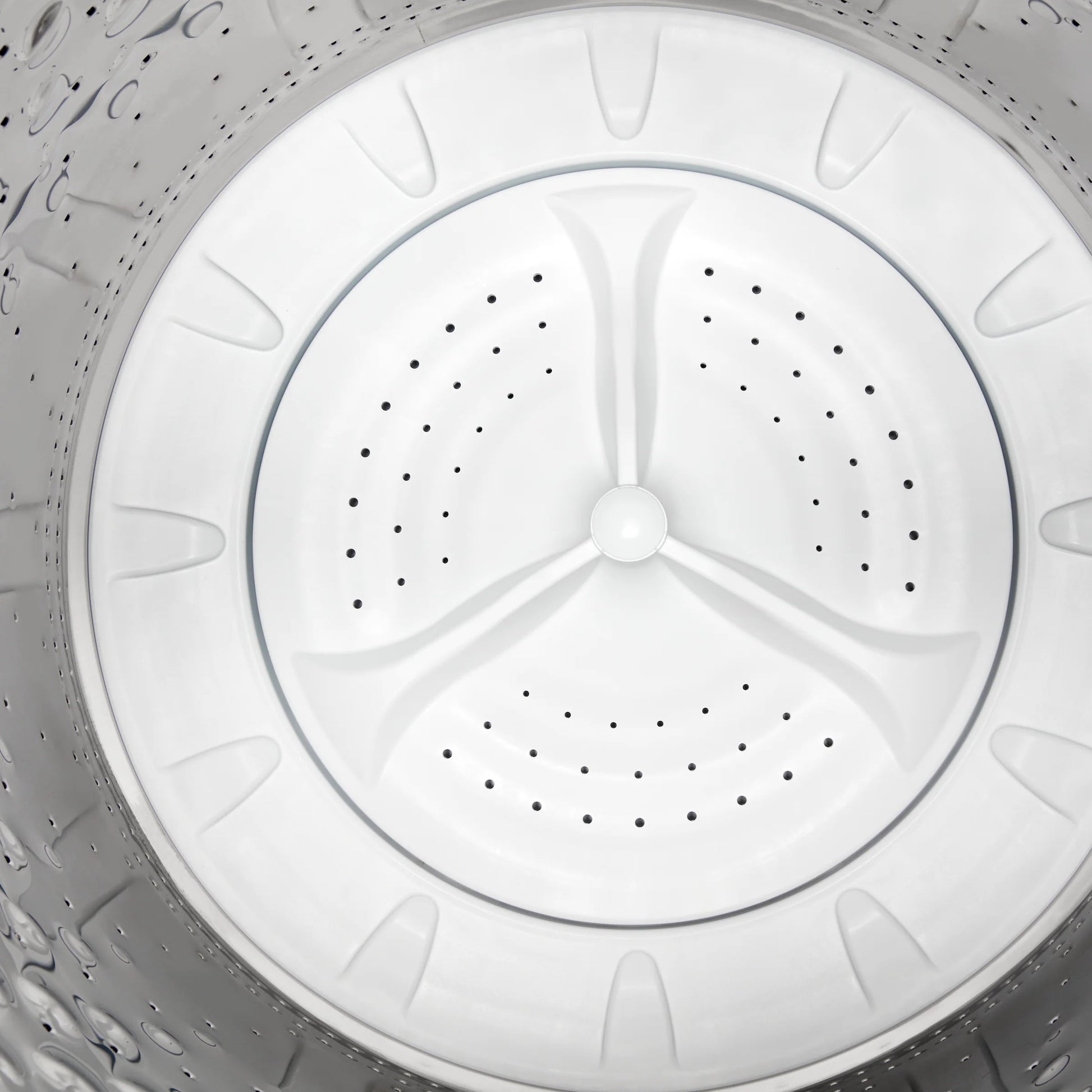 Interior view of a stainless steel washing machine drum with perforated holes and plastic agitator in home appliance collection