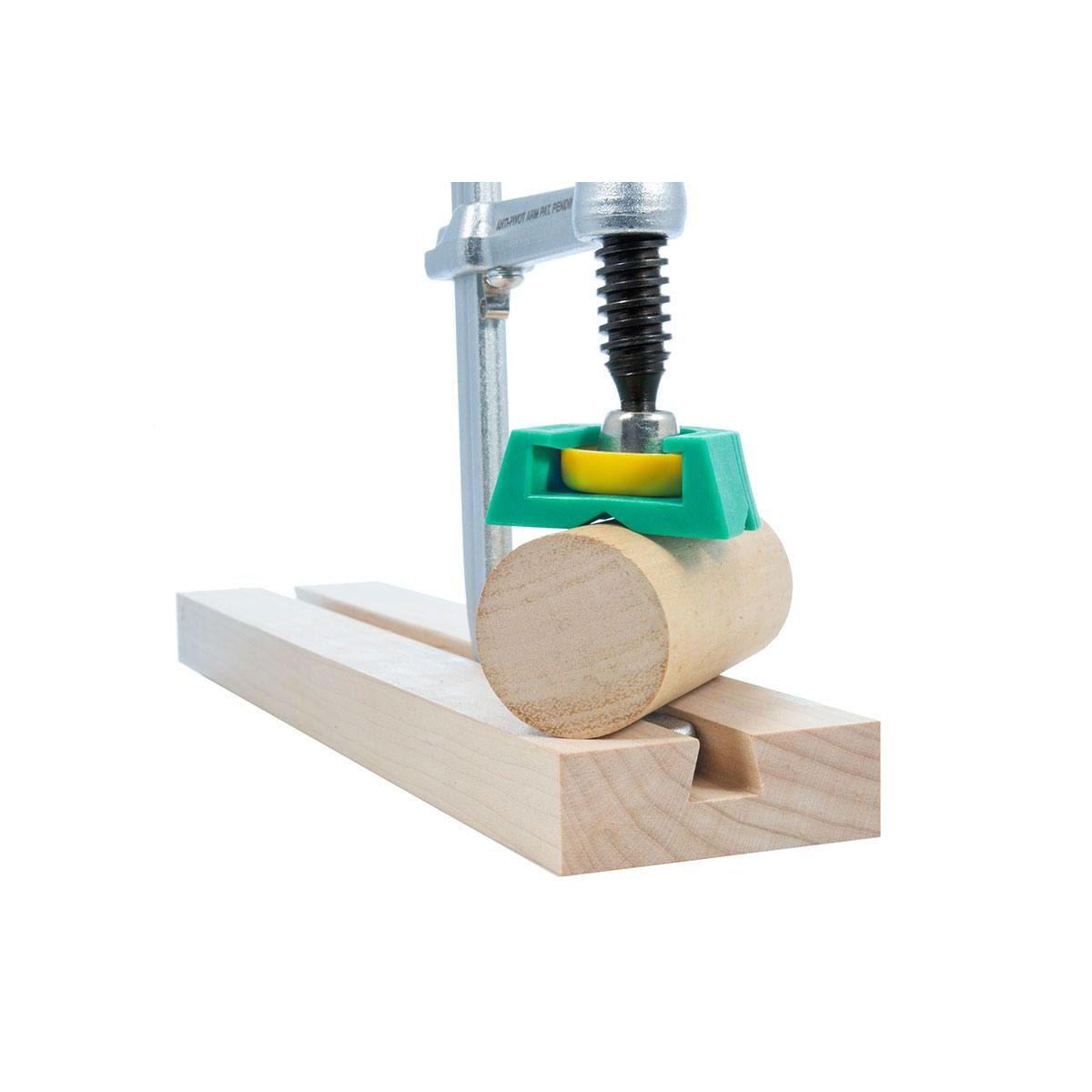 Close-up of a metal clamp with green and yellow plastic parts securing a round wooden dowel in a wooden dovetail track for woodworking.