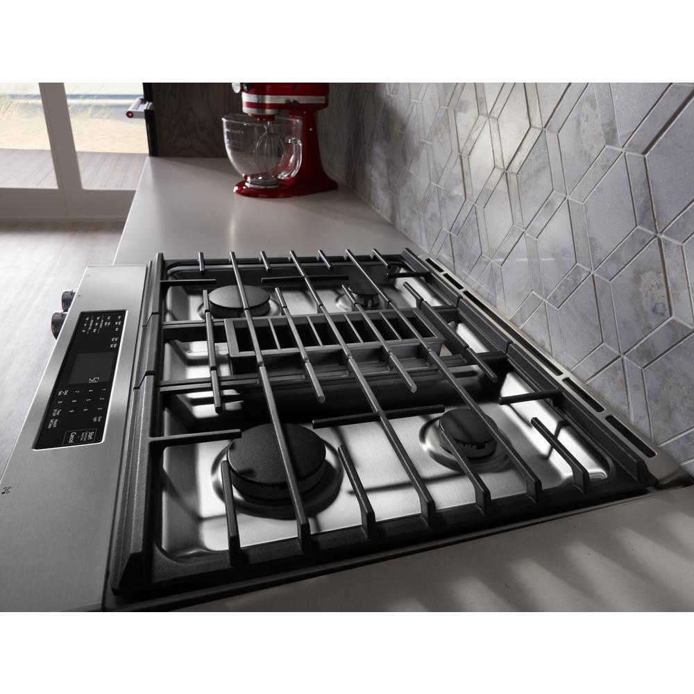 Stainless steel four-burner dual fuel range with integrated downdraft ventilation in modern kitchen setting