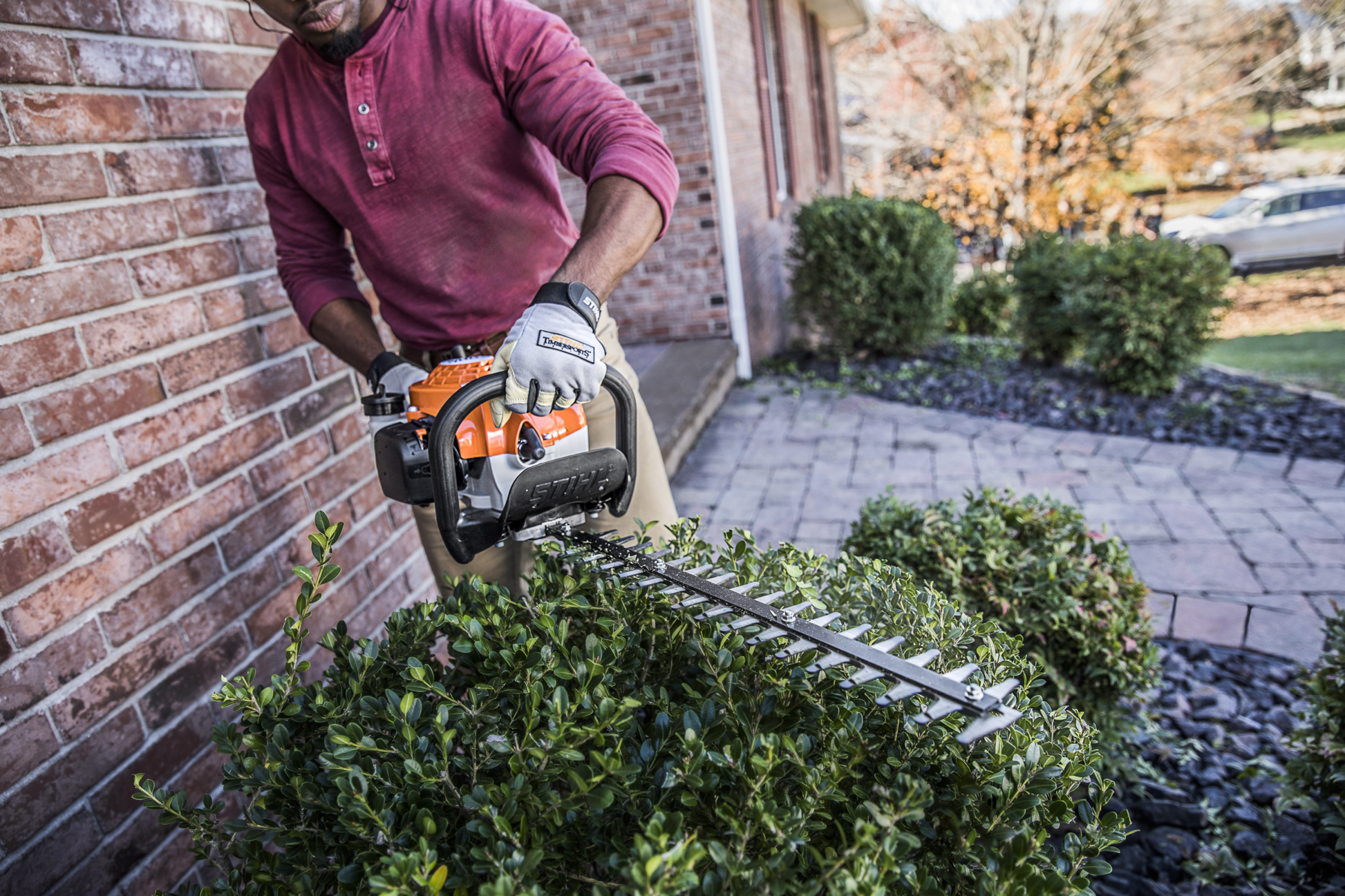 Man trimming outdoor greenery with lightweight orange and white hedge trimmer for home improvement tasks