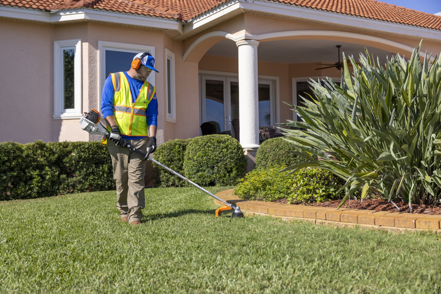 Man wearing safety gear operating a loop-handle gas trimmer for precise yard edge trimming near landscaping