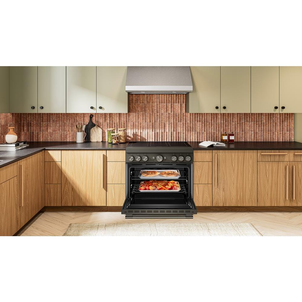 Contemporary kitchen with open black induction range oven baking pizza and roasted vegetables in wood and cream cabinetry setting