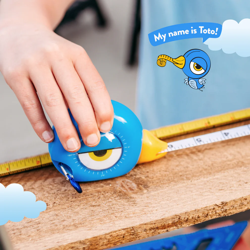 Child’s hand using a blue bird-shaped measuring tape from the Toys & Games collection on wood surface