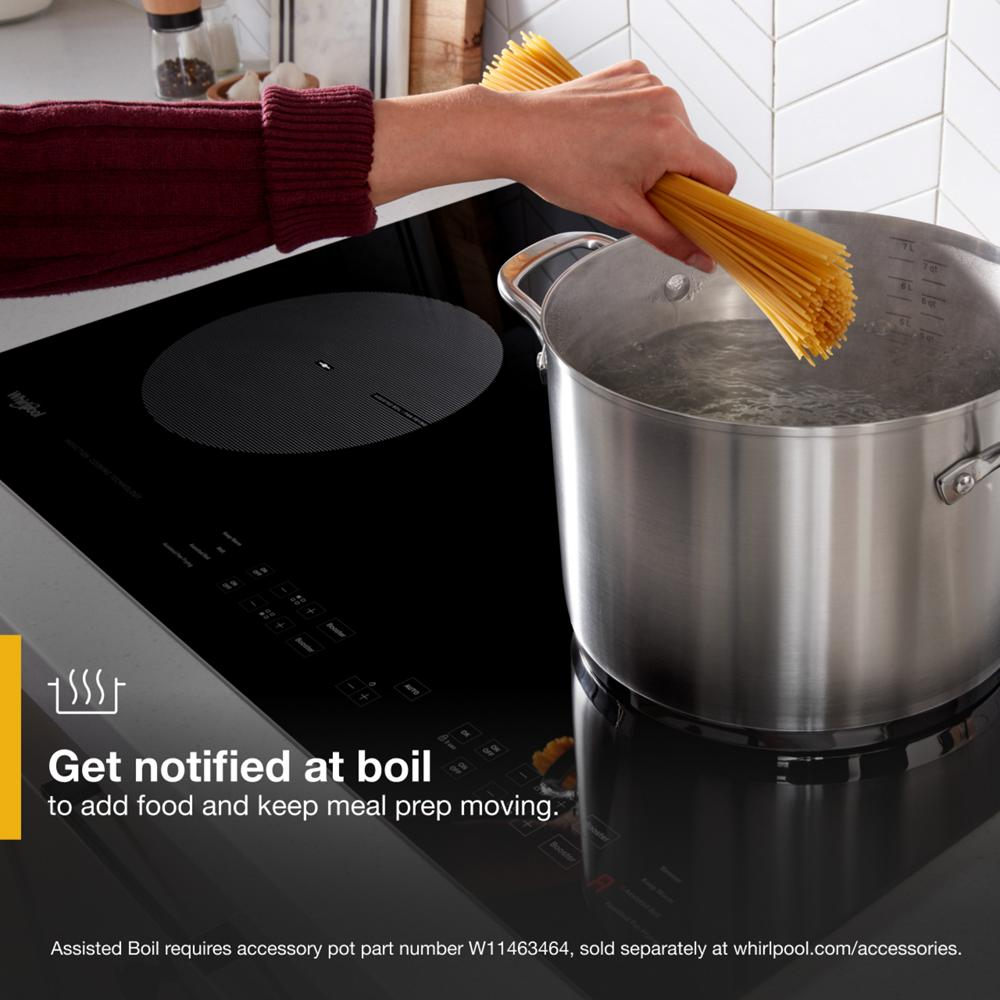 Hand adding dry spaghetti to boiling water in large stainless steel pot on sleek black induction cooktop