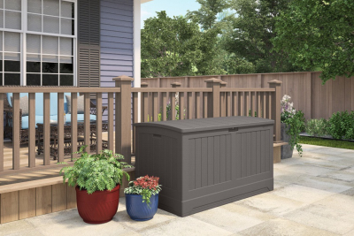 Dark gray resin outdoor storage chest with vertical paneling on a patio surrounded by lawn and garden decor