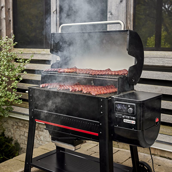 Black pellet grill with open lid showing ribs cooking on dual racks while smoke rises, designed for outdoor cooking and grilling enthusiasts.