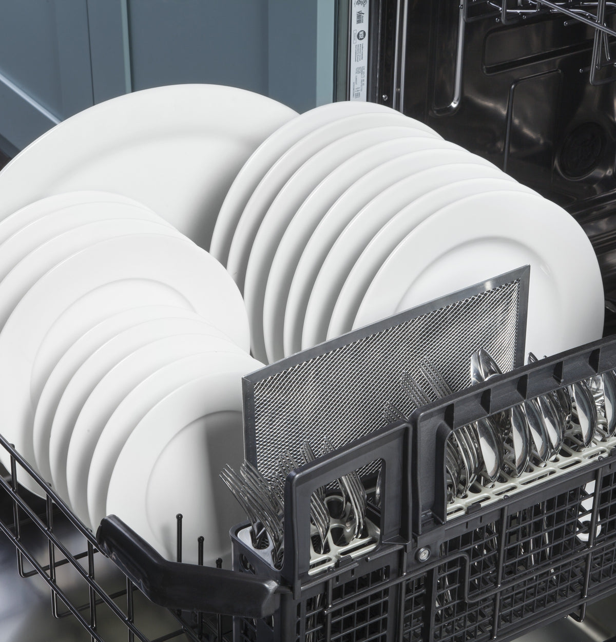 Dishwasher lower rack loaded with white plates and silverware in a kitchen appliance setting for home improvement.