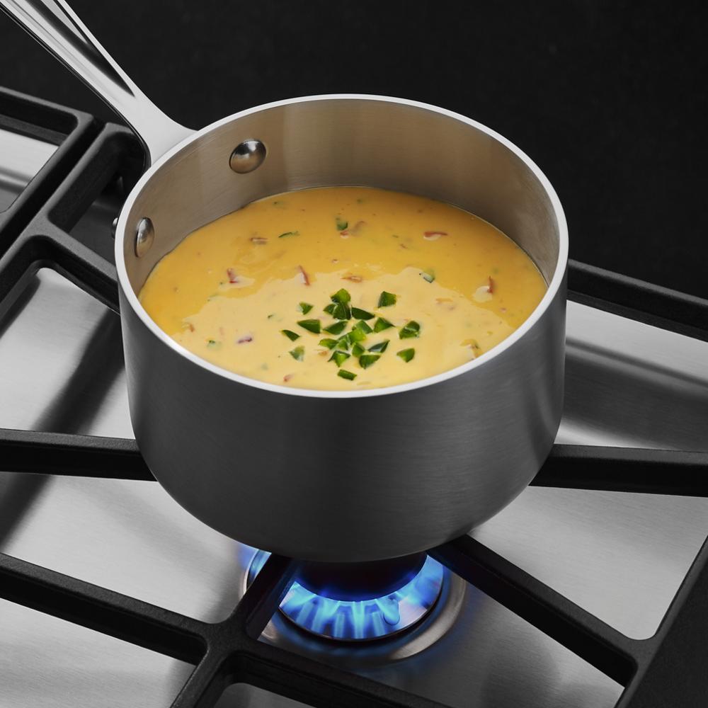 Saucepan with creamy soup simmering on blue flame of stainless steel gas cooktop in kitchenware and appliances collection