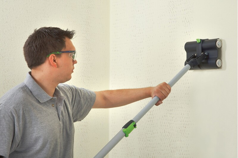 Man using drywall sander with extended handle to smooth wall surface in power tool accessories for home improvement