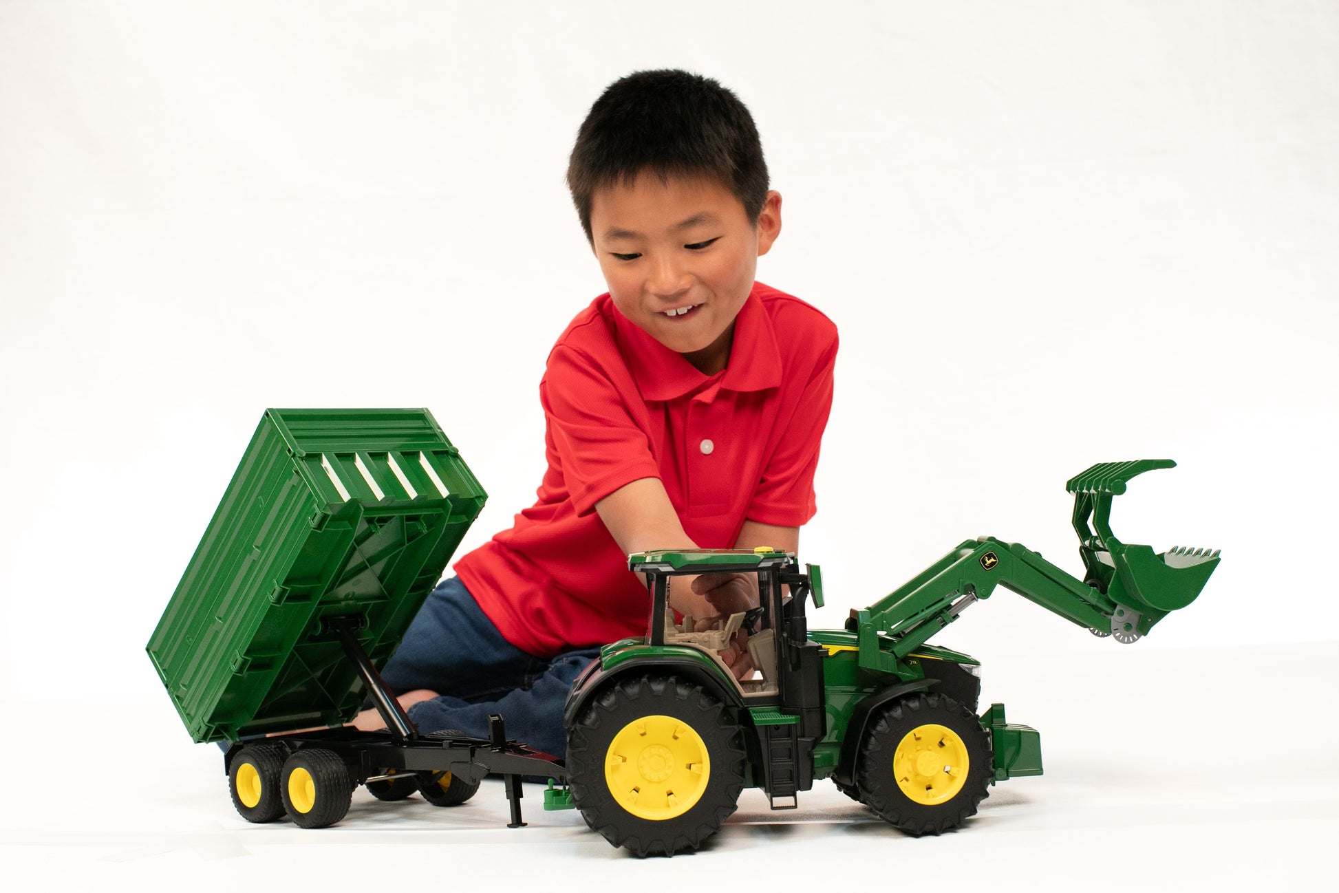 Child playing with green toy tractor featuring front loader and articulated tipping trailer for imaginative play
