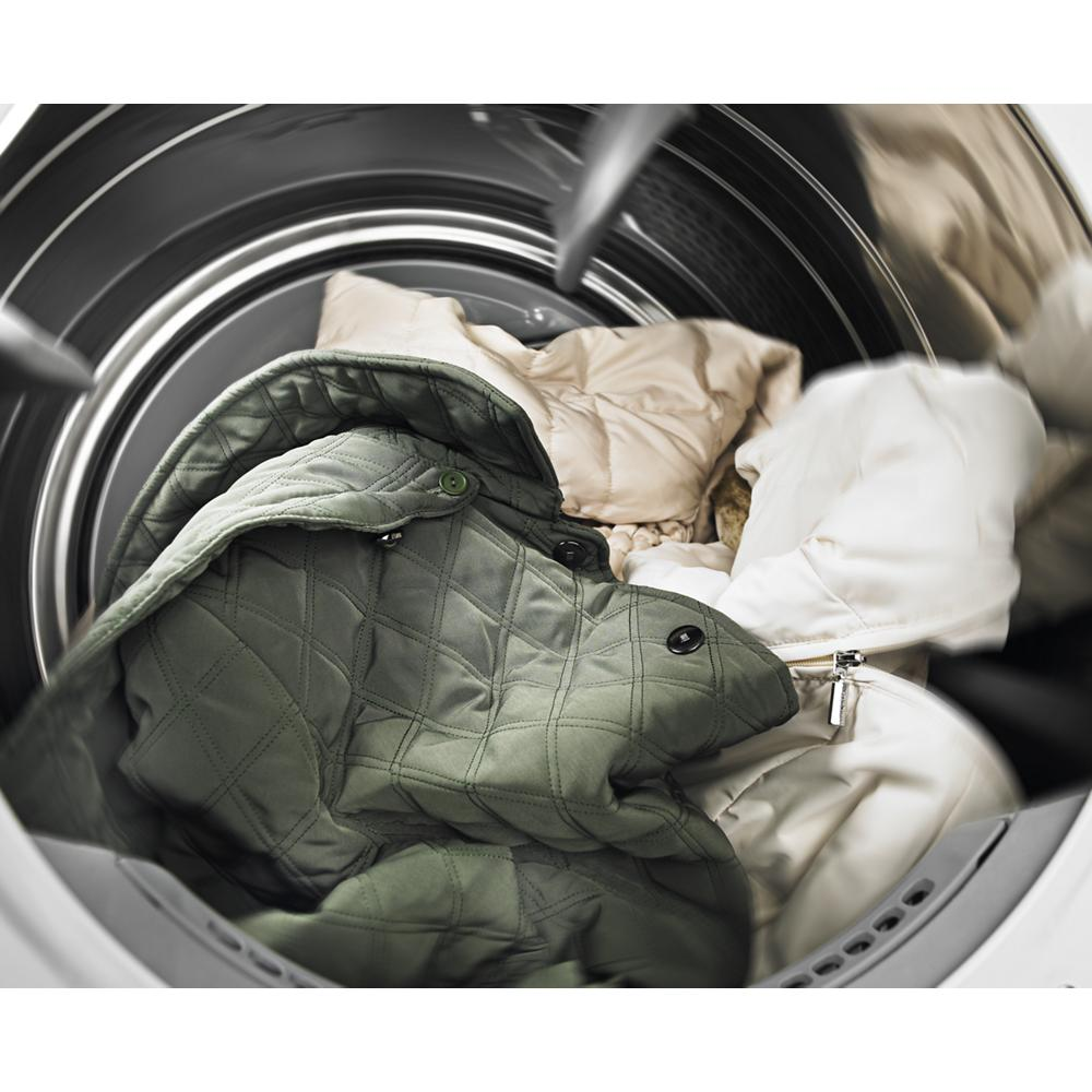 Clothes including a green quilted jacket tumbling inside a front load washing machine in appliances category