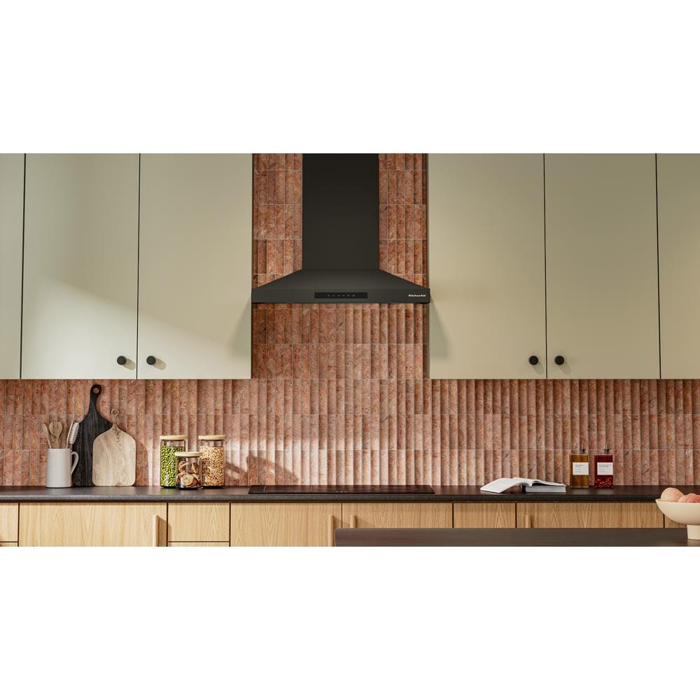 Matte black wall-mount canopy hood above cooktop in modern kitchen with textured brown tile backsplash and wood cabinetry