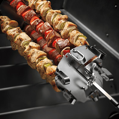 Close-up of six stainless steel skewers securing seasoned meat and vegetables on a rotisserie grill attachment