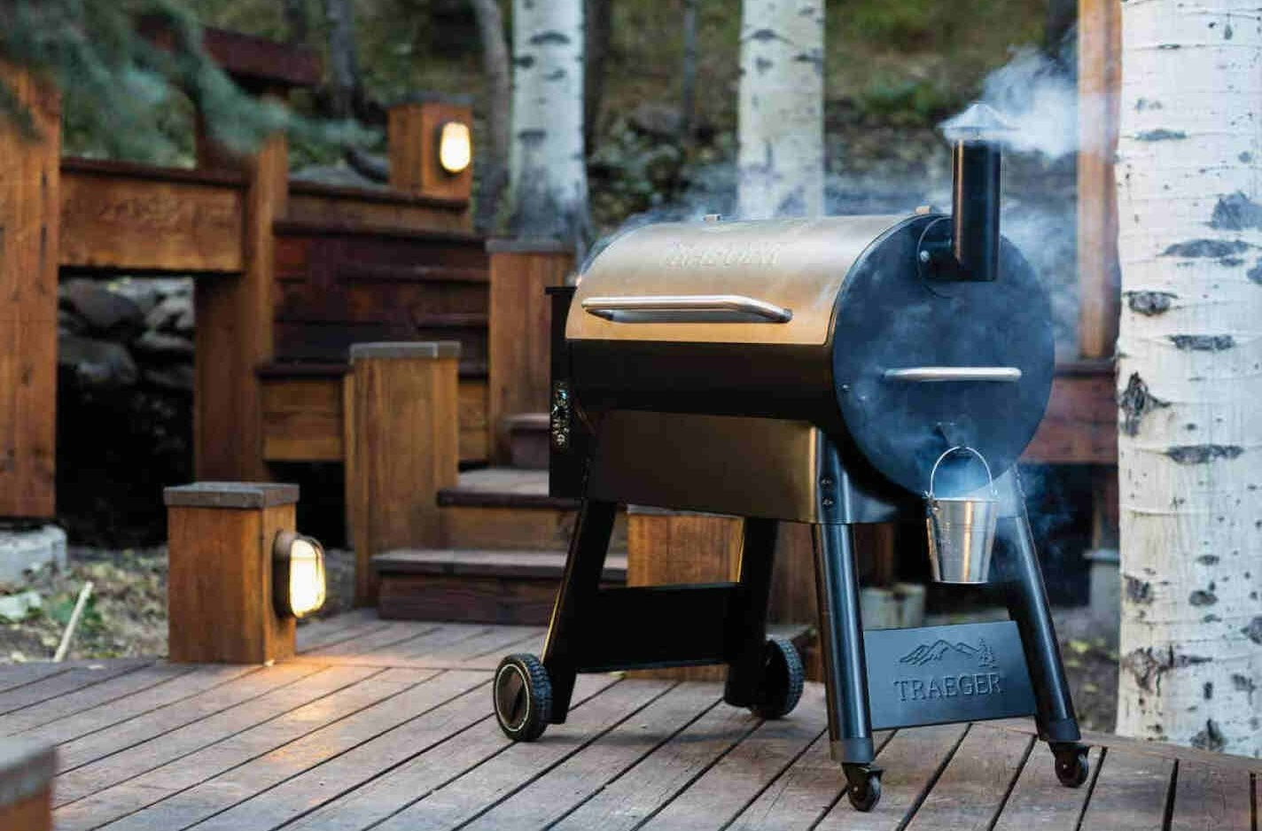 Bronze and black wood pellet grill emitting smoke on outdoor wooden deck in natural forest setting