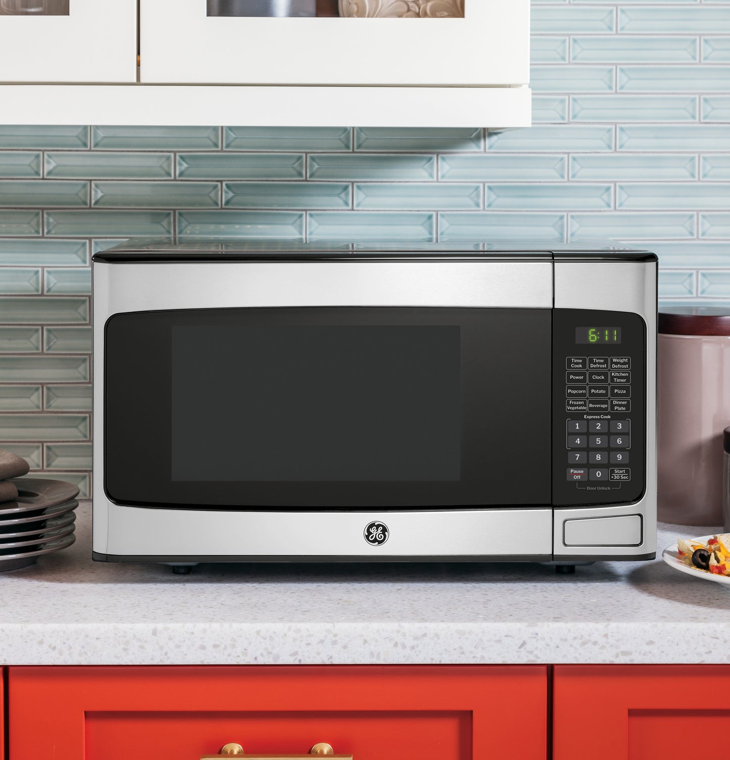 Countertop stainless steel microwave oven with digital keypad and green LED clock in modern kitchen setting