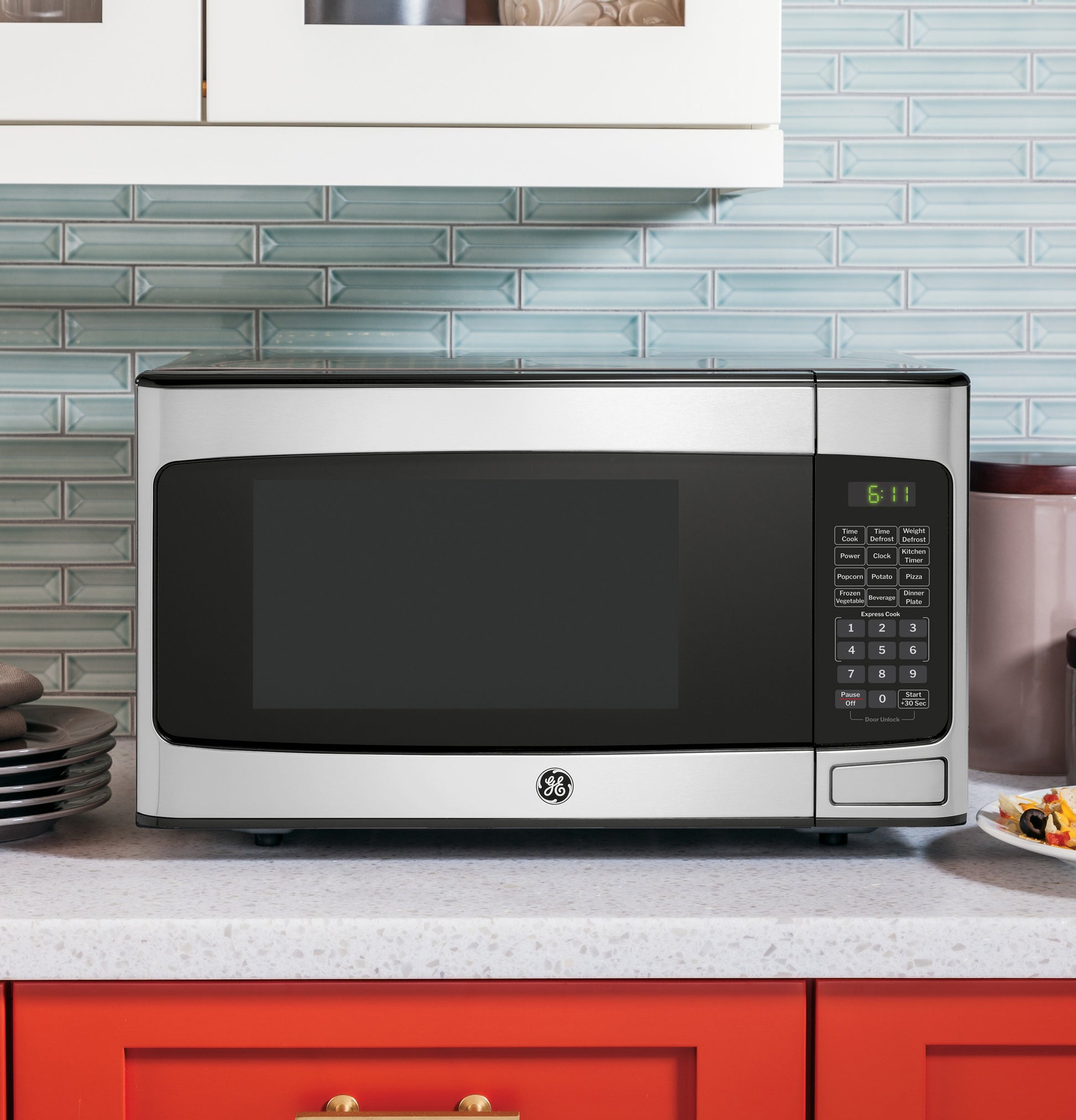 Countertop stainless steel microwave oven with digital keypad and green LED clock in modern kitchen setting