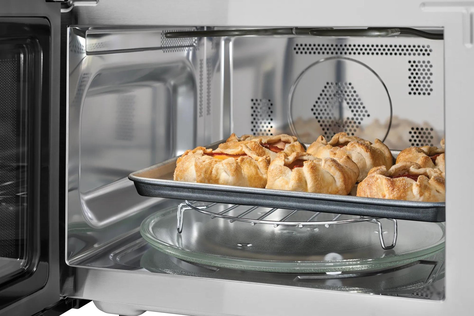 Interior view of a built-in side swing microwave oven with a baking tray of browned pastries cooking inside