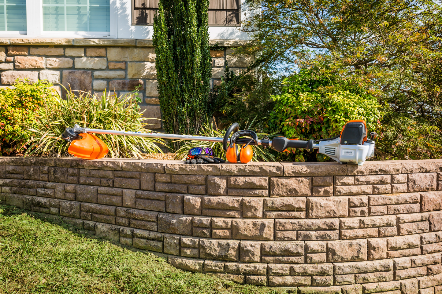 Orange and silver straight shaft string trimmer resting on retaining wall for home improvement and landscaping tasks