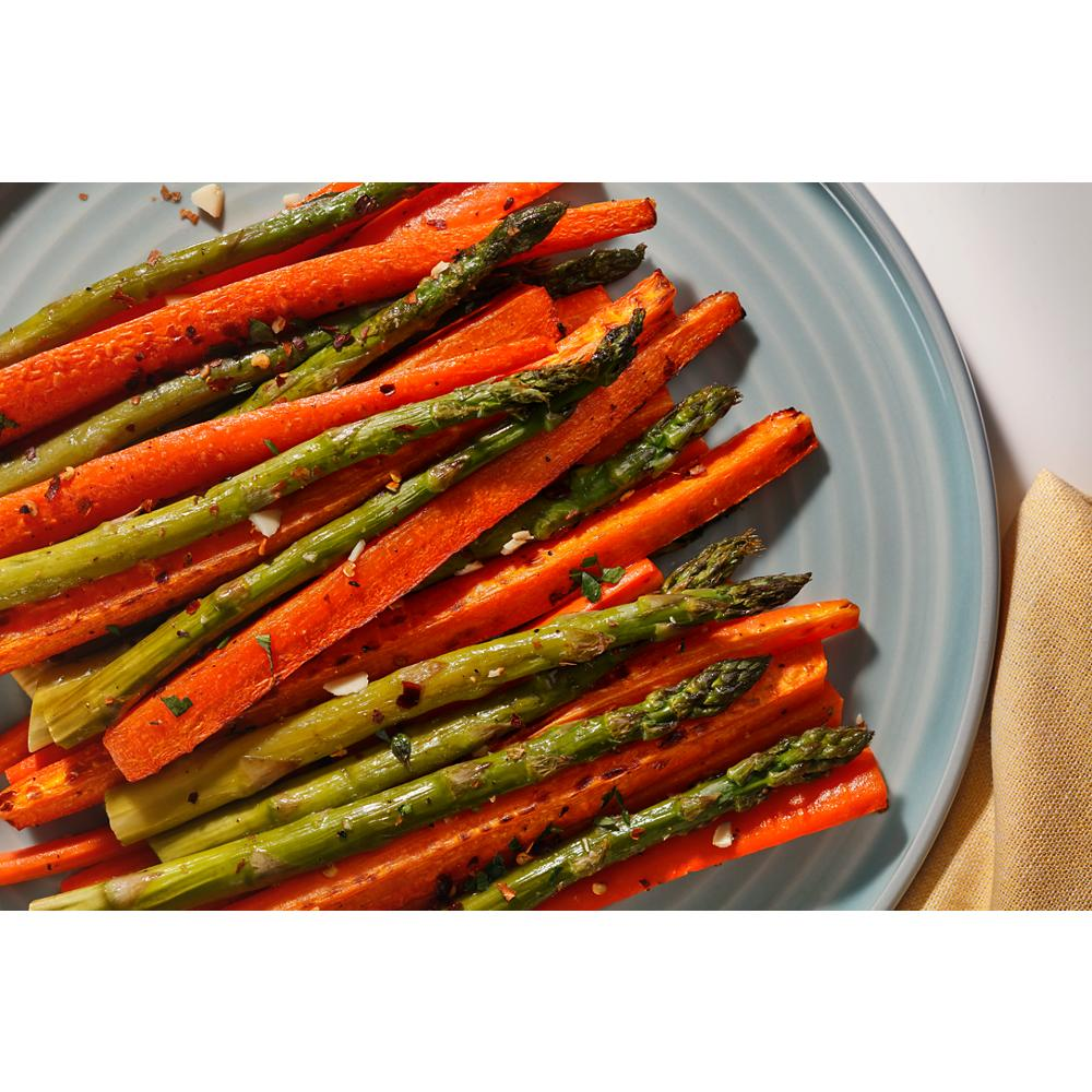Roasted asparagus and carrot sticks seasoned with herbs on a light blue plate in kitchenware setting