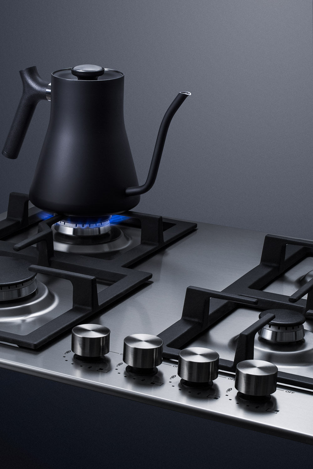 Black gooseneck kettle heating on stainless steel four-burner propane gas cooktop from kitchenware collection