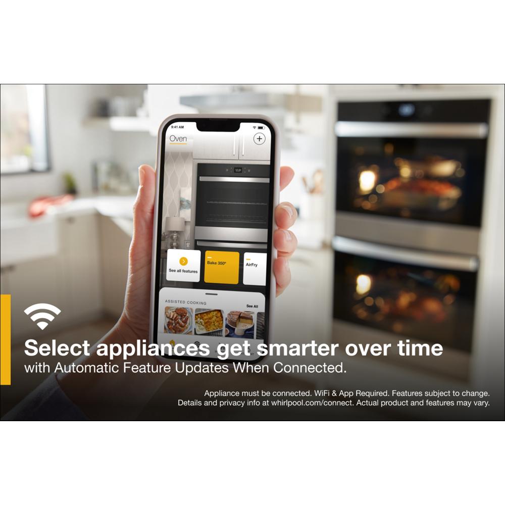 Hand holding phone displaying smart oven controls with double wall ovens in kitchen appliance setting