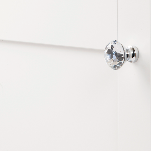 Clear faceted glass knob with chrome base installed on white cabinet door for furniture hardware and home improvement