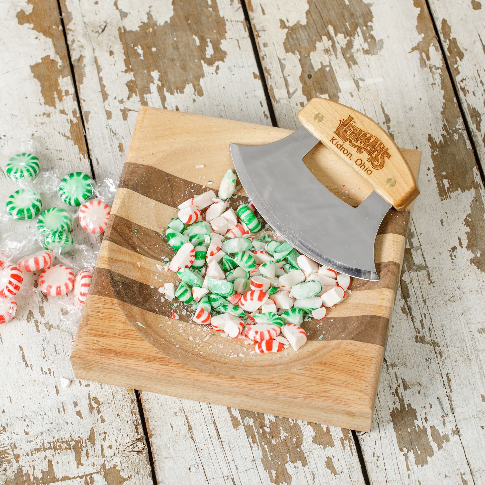 Wood-handled ulu knife with engraved logo on striped wooden bowl crushing green and red peppermint candies in kitchenware collection