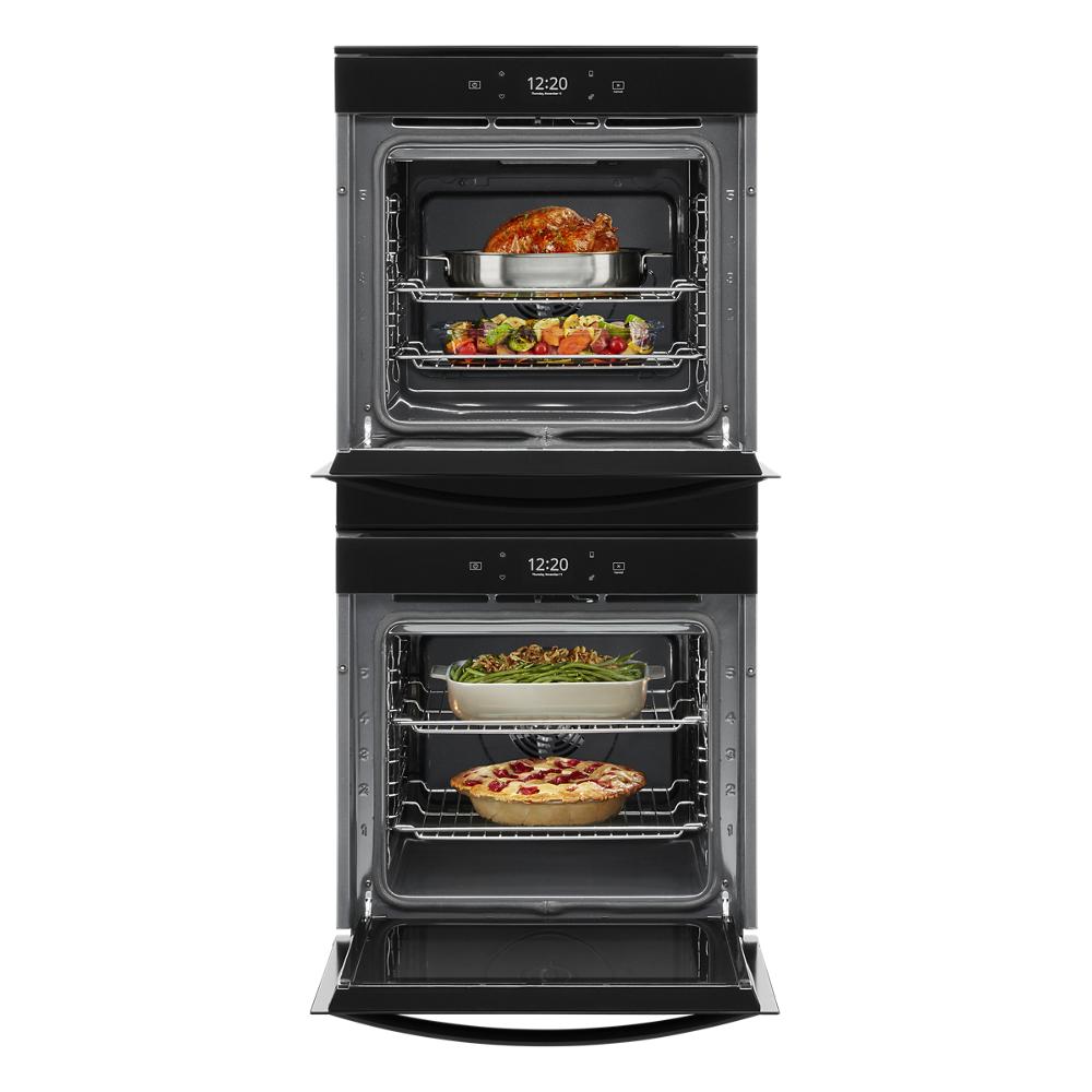 Open double wall oven with multiple dishes cooking on racks inside stainless steel kitchen appliance