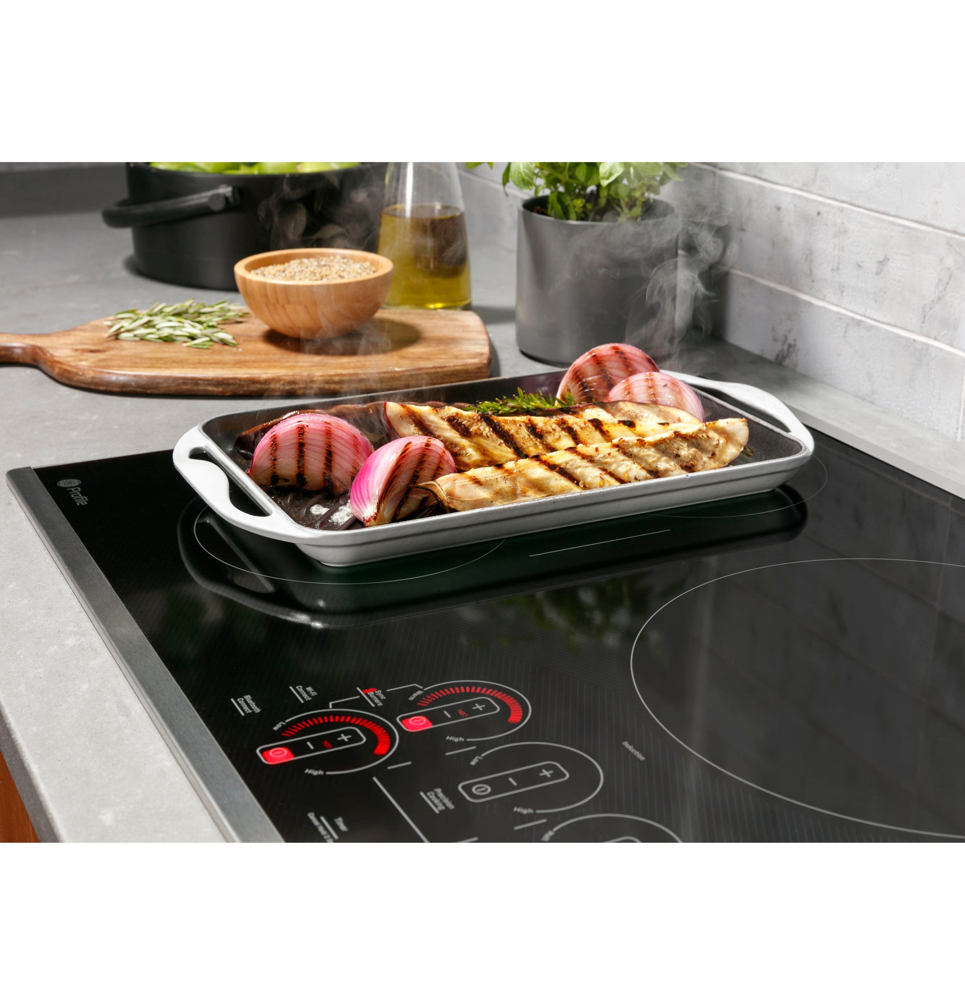 White grill pan with cooked chicken and onions steaming on black touch control induction cooktop in modern kitchen