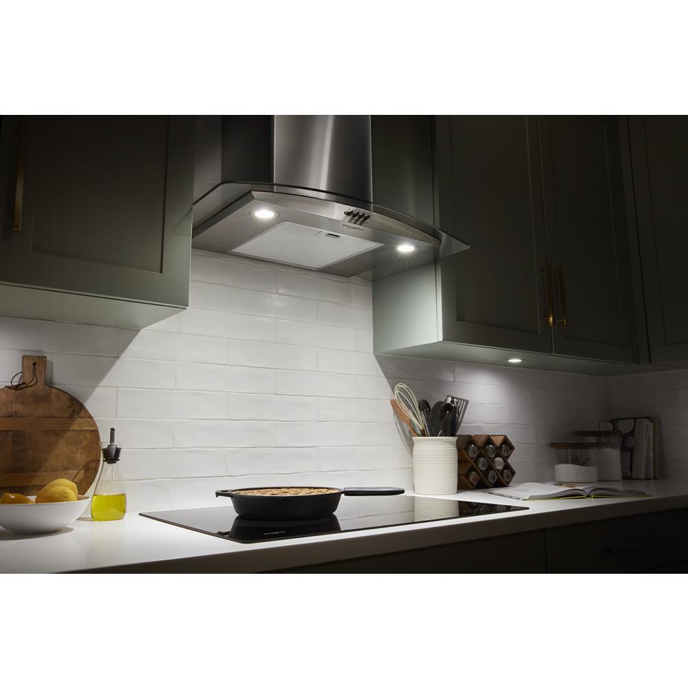 Wall mounted stainless steel chimney range hood with LED lights above white countertop and kitchenware in modern kitchen