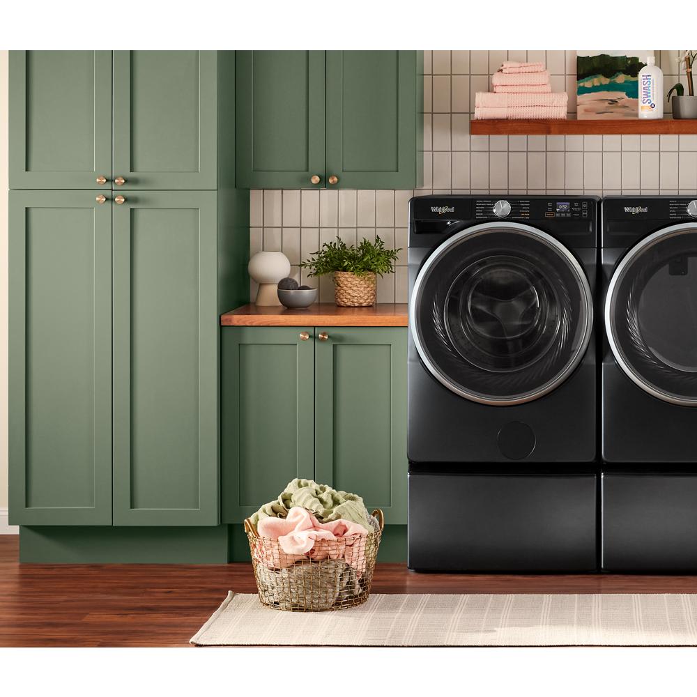 Black smart front load washer and dryer set with digital controls beside green cabinetry in laundry room setting