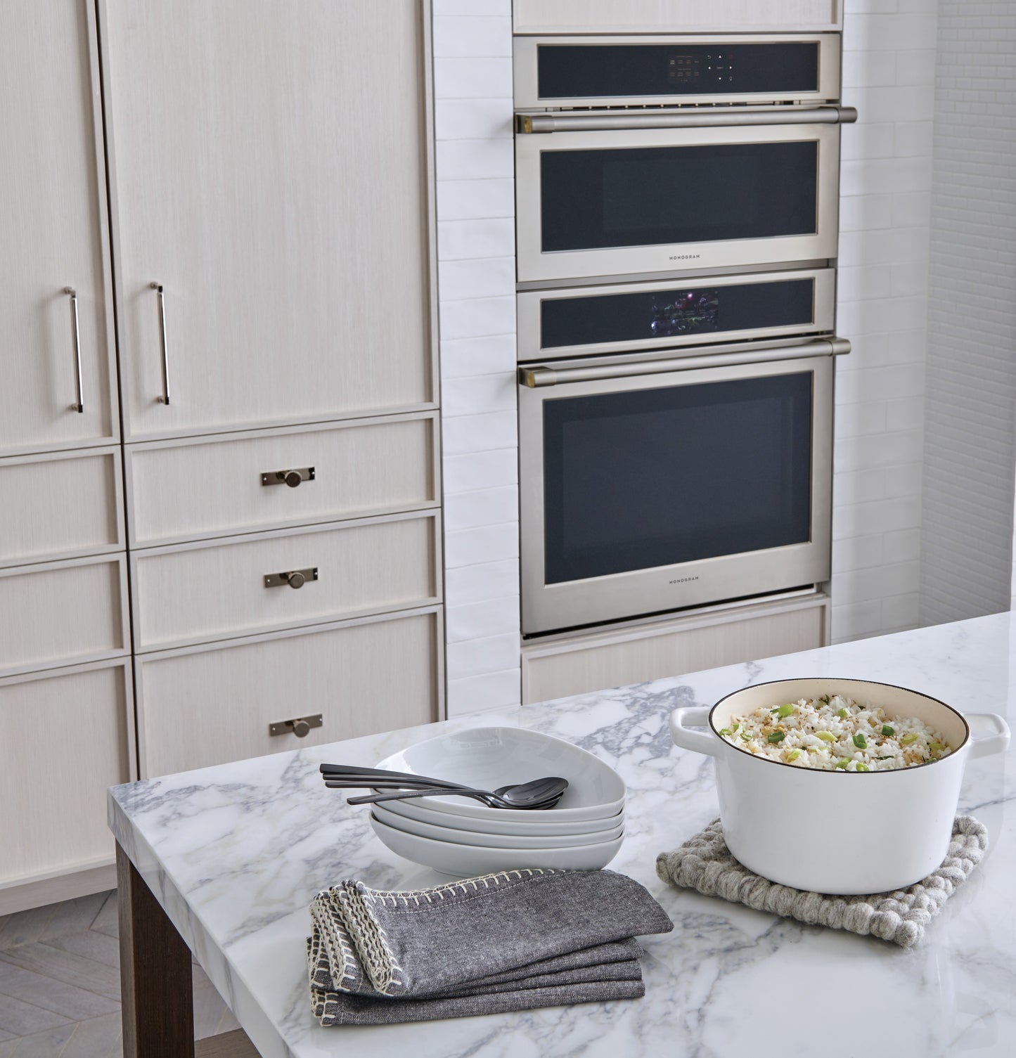 White kitchen with built-in stainless steel ovens and marble island featuring cookware and dishware in appliances collection
