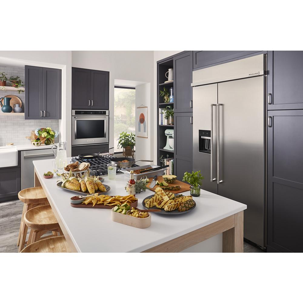 Contemporary kitchen with stainless steel refrigerator, dark gray cabinets, white island, wooden stools, and food platters on countertop