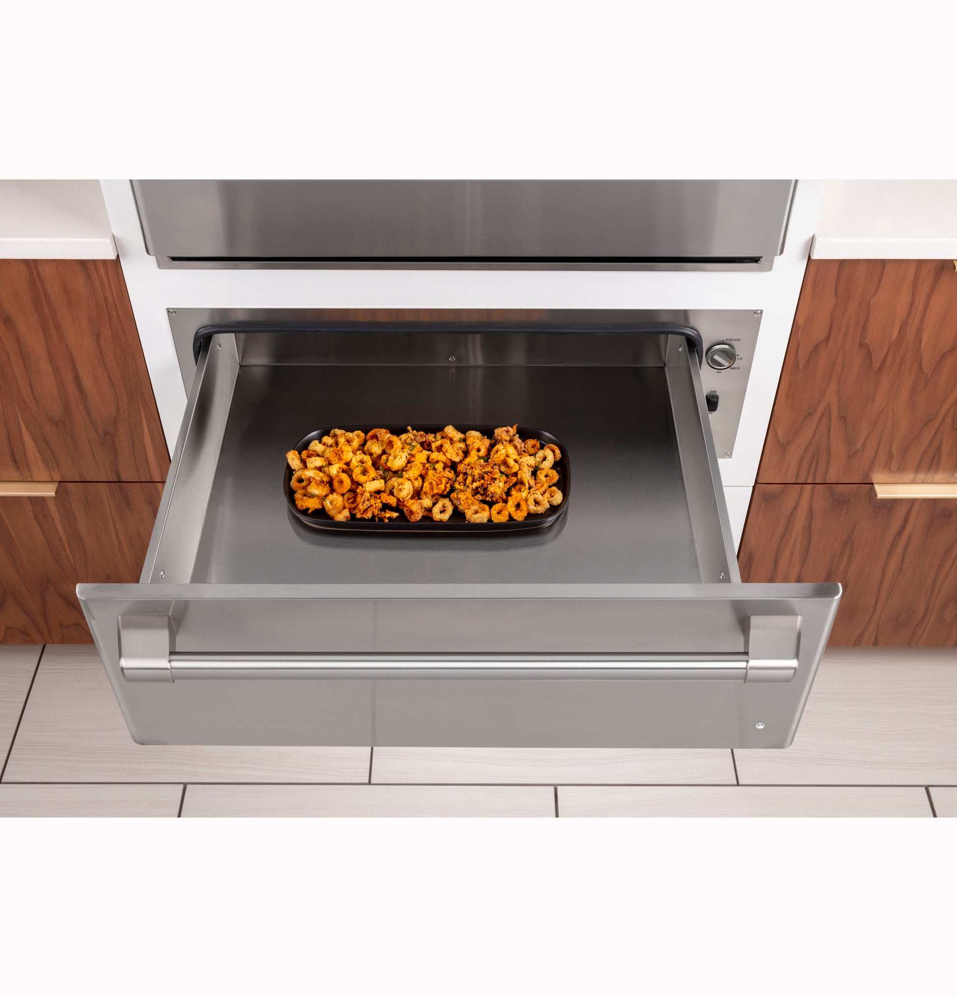 Stainless steel warming drawer from appliances collection with open drawer holding tray of cooked pasta inside kitchen setting