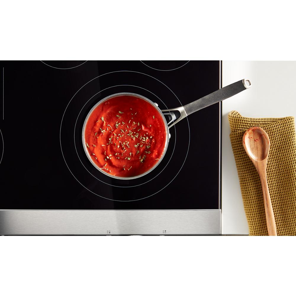 Overhead view of saucepan with tomato sauce and herbs on glass electric cooktop from Ranges collection