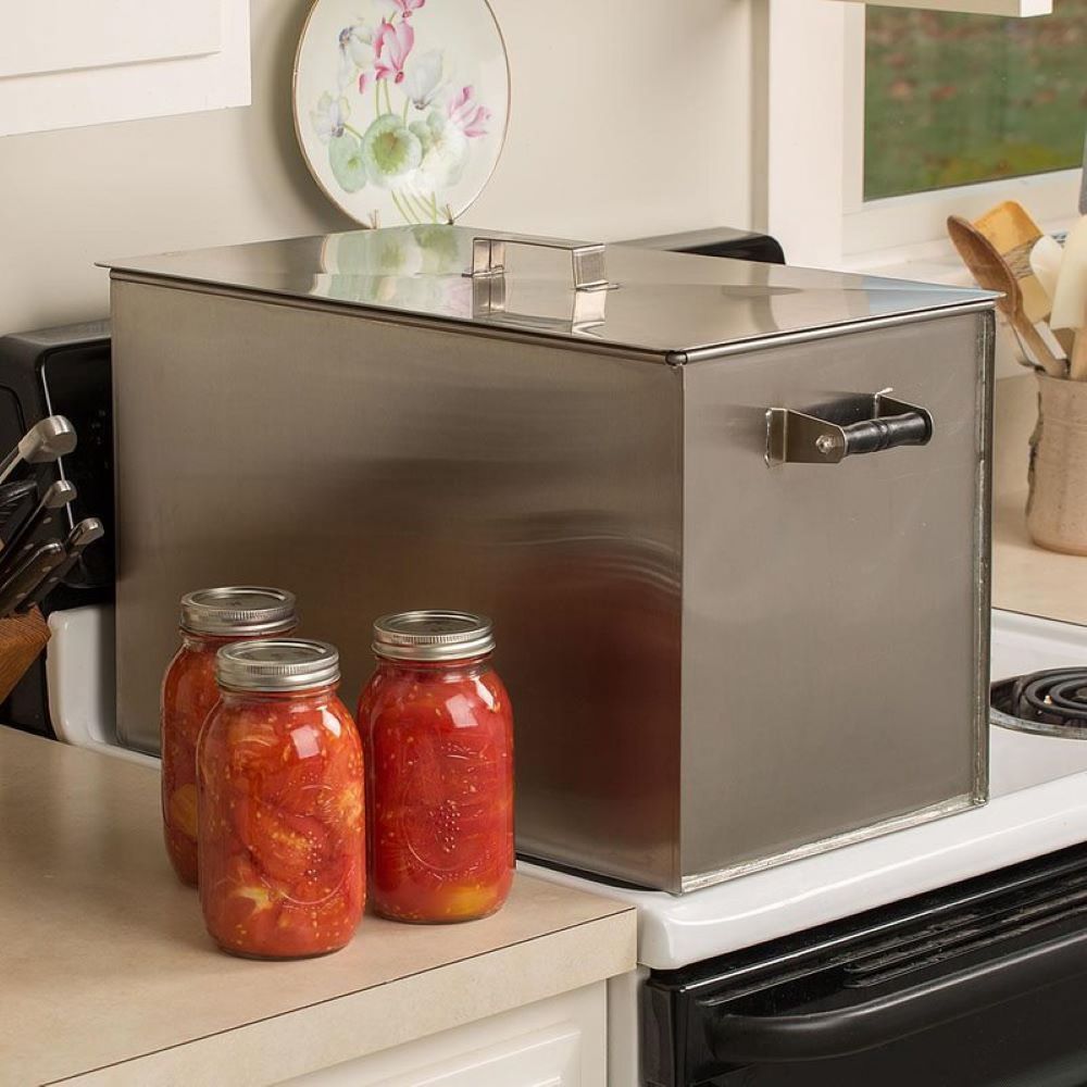 Stainless steel stovetop water bath canner beside three glass jars filled with preserved tomatoes for kitchenware collections
